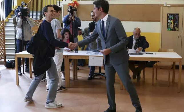 French Prime Minister Gabriel Attal, right, shakes hands with a voter during the second round of the legislative elections, Sunday, July 7, 2024 in Vanves, outside Paris. Voting has begun in mainland France on Sunday in pivotal runoff elections that could hand a historic victory to Marine Le Pen's far-right National Rally and its inward-looking, anti-immigrant vision — or produce a hung parliament and years of political deadlock. (Alain Jocard, Pool via AP)