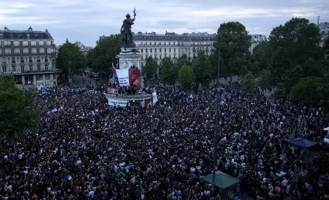 People stand in Republique Plaza as they react to the projection of results during the second round of the legislative elections, in Paris, France. Polls have closed in France, and polling projections say a coalition on the left that came together unexpectedly has won the most parliamentary seats in the pivotal runoff elections after a high turnout among voters. (AP Photo/Christophe Ena)