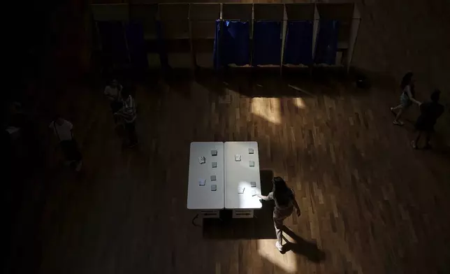 A woman picks up ballots at a polling station to vote in the second round of the legislative elections, in Lyon, central France, Sunday, July 7, 2024. France votes Sunday in pivotal runoff elections that could hand a historic victory to Marine Le Pen's far-right National Rally and its inward-looking, anti-immigrant vision — or produce a hung parliament and years of political deadlock. (AP Photo/Laurent Cipriani)