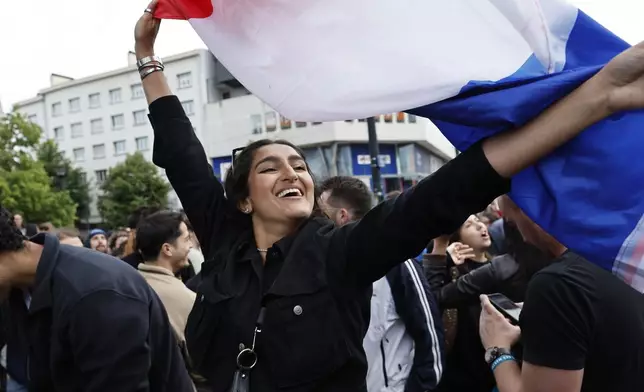 A woman waves the French flag as she reacts to projected results after the second round of the legislative elections, Sunday, July 7, 2024 in Nantes, western France. Polls have closed in France, and polling projections say a coalition on the left that came together unexpectedly has won the most parliamentary seats in the pivotal runoff elections after a high turnout among voters. (AP Photo/Jeremias Gonzalez)