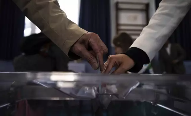 A voter, left, casts his ballot for the second round of the legislative elections, Sunday, July 7, 2024 in Paris. France votes Sunday in pivotal runoff elections that could hand a historic victory to Marine Le Pen's far-right National Rally and its inward-looking, anti-immigrant vision — or produce a hung parliament and years of political deadlock. (AP Photo/Louise Delmotte)