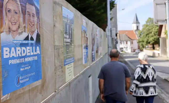 A couple walks past electoral posters showing far-right leaders Marine Le Pen and Jordan Bardella during second round of the legislative elections, Sunday, July 7, 2024 in Mittelschaeffolsheim , eastern France. France votes Sunday in pivotal runoff elections that could hand a historic victory to Marine Le Pen's far-right National Rally and its inward-looking, anti-immigrant vision — or produce a hung parliament and years of political deadlock. (AP Photo/Jean-Francois Badias)