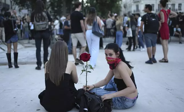 Two women sit on either side of a rose as people react to projected results after the second round of the legislative elections, in Lyon, central France, Sunday, July 7, 2024. Polls have closed in France, and polling projections say a coalition on the left that came together unexpectedly has won the most parliamentary seats in the pivotal runoff elections after a high turnout among voters. (AP Photo/Laurent Cipriani)