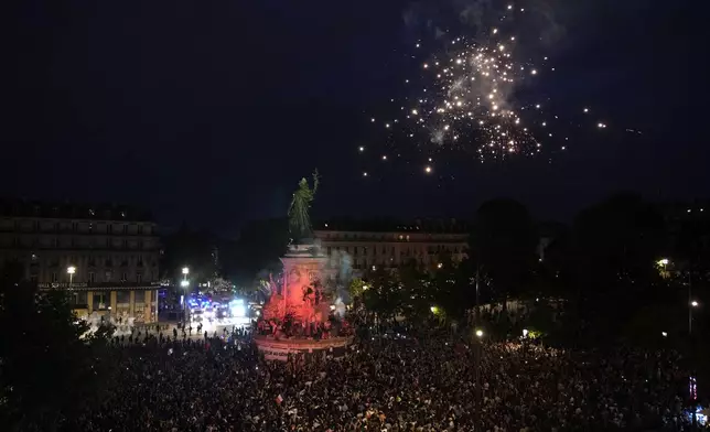 Fireworks go off as people stand in Republique Plaza and react to the projection of results during the second round of the legislative elections, in Paris, France, Sunday, July 7, 2024. Polls have closed in France, and polling projections say a coalition on the left that came together unexpectedly has won the most parliamentary seats in the pivotal runoff elections after a high turnout among voters. (AP Photo/Christophe Ena)