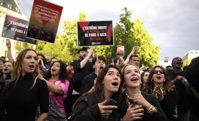 People react to the projection of results during the second round of the legislative elections, near Republique Plaza in Paris, France, Sunday, July 7, 2024. Polls have closed in France, and polling projections say a coalition on the left that came together unexpectedly has won the most parliamentary seats in the pivotal runoff elections after a high turnout among voters. Sign reads "The extreme right shall not pass. From Gaza to Paris Intifada". (AP Photo/Christophe Ena)