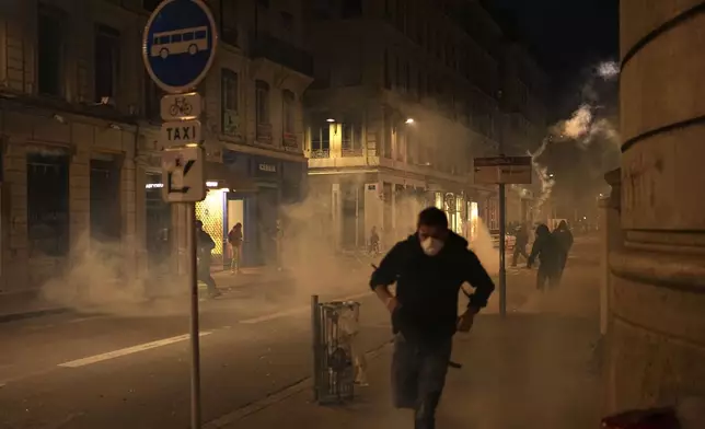 Demonstrators run from smoke flares during reactions to projected results after the second round of the legislative elections, in Lyon, central France, Sunday, July 7, 2024. Polls have closed in France, and polling projections say a coalition on the left that came together unexpectedly has won the most parliamentary seats in the pivotal runoff elections after a high turnout among voters. (AP Photo/Laurent Cipriani)