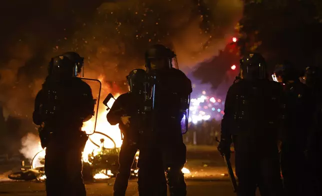 Police officers stand by burning bicycles during tensions near Republique plaza following the second round of the legislative elections, Sunday, July 7, 2024, in Paris. A coalition of the French left that quickly banded together to beat a surging far right in legislative elections won the most seats in parliament but not a majority, according to polling projections Sunday, a stunning outcome that threatens to plunge the country into political and economic turmoil. (AP Photo/Aurelien Morissard)