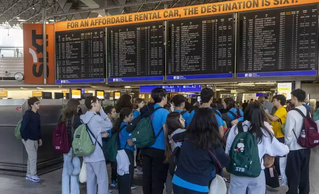 Travelers stand in front of a display board in the terminal at Frankfurt Airport in Frankfurt, Germany Thursday, July 25, 2024. Flights at the airport were suspended temporarily Thursday as climate activists glued themselves to the ground inside the airport grounds, authorities said. (Helmut Fricke/dpa via AP)