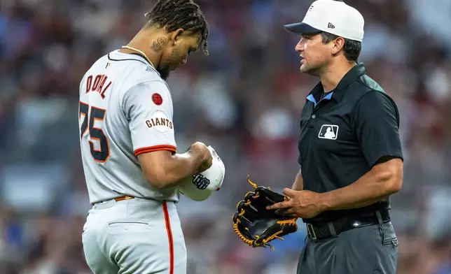 San Francisco Giants pitcher Camilo Doval (75) has his cap and glove checked by umpire Tony Randazzo, right, during the ninth inning of a baseball game against the Atlanta Braves, Thursday, July 4, 2024, in Atlanta. (AP Photo/Jason Allen)