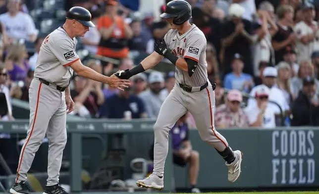 San Francisco Giants third base coach Matt Williams, left, congratulates Tyler Fitzgerald as he circles the bases after hitting a solo home run off Colorado Rockies starting pitcher Kyle Freeland in the third inning of a baseball game, Saturday, July 20, 2024, in Denver. (AP Photo/David Zalubowski)