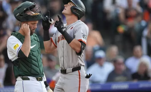 San Francisco Giants' Tyler Fitzgerald, front, gestures as he crosses home plate after hitting a solo home run as Colorado Rockies catcher Jacob Stallings looks on in the third inning of a baseball game Saturday, July 20, 2024, in Denver. (AP Photo/David Zalubowski)
