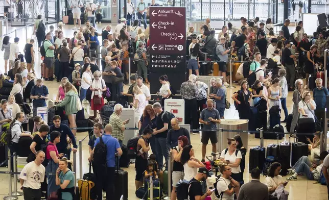 Passengers wait in front of check-in counters at the capital's Berlin Brandenburg Airport, in Schönefeld, Germany, Friday, July 19, 2024, after a widespread technology outage disrupted flights, banks, media outlets and companies around the world. (Christoph Soeder/dpa via AP)