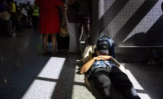 A passenger takes a nap inside a terminal at Harry Reid International Airport on Friday, July 19, 2024, after a faulty CrowdStrike update caused a major internet outage for computers running Microsoft Windows. (AP Photo/Ty ONeil)