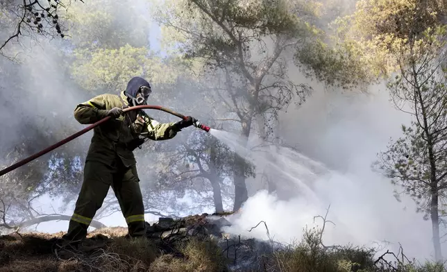A firefighter struggles to extinguish a forest fire in the Keratea area, southeast of Athens, Greece, Sunday, June 30, 2024. Two large wildfires were burning Sunday near Greece's capital of Athens, and authorities sent emergency messages for some residents to evacuate and others to stay at home and close their windows to protect themselves from smoke. (AP Photo/Yorgos Karahalis)
