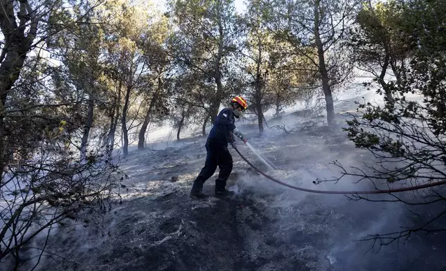 A firefighter tries to extinguish a forest fire in the Keratea area, southeast of Athens, Greece, Sunday, June 30, 2024. Two large wildfires were burning Sunday near Greece's capital of Athens, and authorities sent emergency messages for some residents to evacuate and others to stay at home and close their windows to protect themselves from smoke. (AP Photo/Yorgos Karahalis)