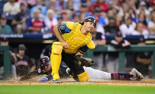 Philadelphia Phillies' J.T. Realmuto, top, fields the ball as Cleveland Guardians' Andrés Giménez, rear, scores on a sacrifice hit by Bo Naylor during the fourth inning of a baseball game, Friday, July 26, 2024, in Philadelphia. (AP Photo/Derik Hamilton)