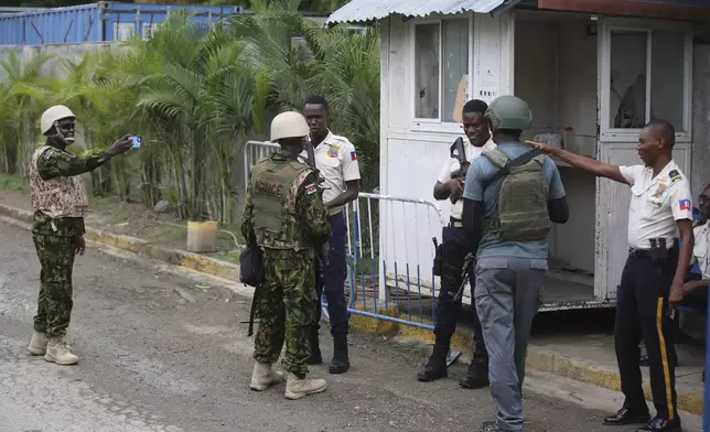 A Kenyan police officer takes candid photos as Haitian and Kenyan police chat with each other at the entrance gate to the General Directorate of Police, in Port-au-Prince, Haiti, Wednesday, July 3, 2024. (AP Photo/Odelyn Joseph)
