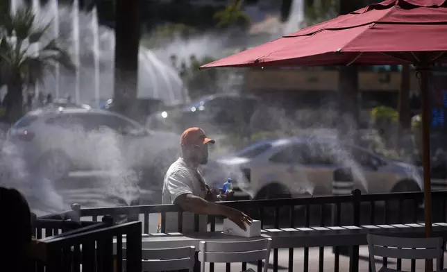 A person cools off in misters along the Las Vegas Strip, Sunday, July 7, 2024, in Las Vegas. A heat wave is spreading across the Western U.S., the National Weather Service said, sending many residents in search of a cool haven from the dangerously high temperatures. (AP Photo/John Locher)