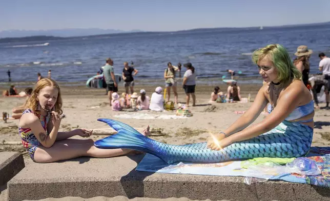 Florence Andersen, 7, eats ice cream while seated next to local mermaid RJ Annest, 16, at Alki Beach, Saturday, July 6, 2024, in Seattle. (Audrey Richardson/The Seattle Times via AP)