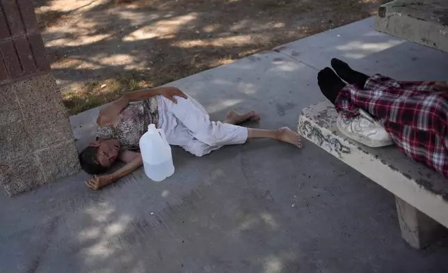 Deb Billet, 66, lies on the ground while Henderson Public Response officers call an ambulance to take her to the hospital for heat-related symptoms Wednesday, July 10, 2024, in Henderson, Nev. Billet has been living on the street. (AP Photo/John Locher)