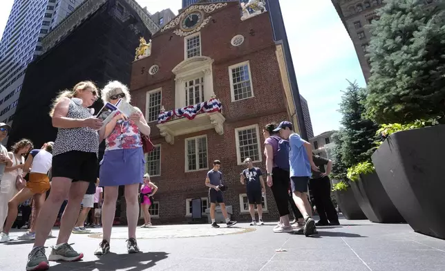 Cathy Nau, front left, and Jackie Trimble, front second left, both of Lake Stevens, Wash., examine maps, Wednesday, July 3, 2024, in front of the Old Statehouse, in Boston. Nau and Trimble visited some of the city's historic sites the day before the July Fourth Independence Day holiday. The Old State House was built in 1713 to replace the original meetinghouse that was destroyed by fire. (AP Photo/Steven Senne)