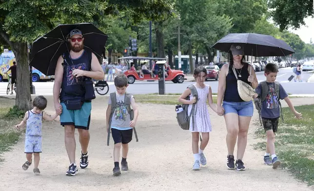 Jordan Savant, second from left, walks with his family carrying umbrellas on the National Mall near the U.S. Capitol, Friday, July 5, 2024, in Washington. (AP Photo/Mariam Zuhaib)