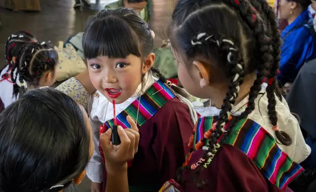 A young exiled Tibetan girl gets her lips painted by her teacher before she performs a traditional dance at an event to celebrate the 89th birthday of Tibetan spiritual leader the Dalai Lama at the Tsuglakhang temple in Dharamshala, India, Saturday, July 6, 2024. (AP Photo/Ashwini Bhatia)