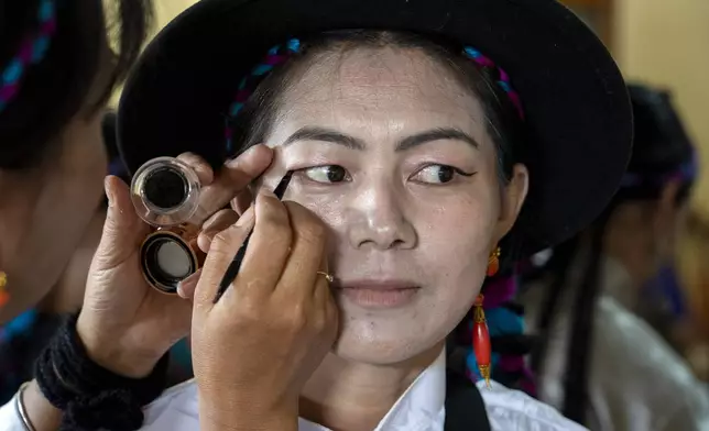 An exiled Tibetan applies eyeliner to another as they wait to perform a traditional dance at an event to celebrate the 89th birthday of Tibetan spiritual leader the Dalai Lama at the Tsuglakhang temple in Dharamshala, India, Saturday, July 6, 2024. (AP Photo/Ashwini Bhatia)