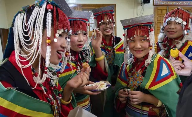 Exiled Tibetan school girls in a traditional costumes eat cakes and sweets as they wait to perform a traditional dance at an event to celebrate the 89th birthday of Tibetan spiritual leader the Dalai Lama at the Tsuglakhang temple in Dharamshala, India, Saturday, July 6, 2024. (AP Photo/Ashwini Bhatia)