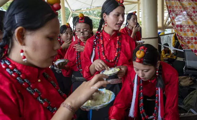 Exiled Tibetans in a ceremonial outfits eat cakes as they wait to perform a traditional dance at an event to celebrate the 89th birthday of Tibetan spiritual leader the Dalai Lama at the Tsuglakhang temple in Dharamshala, India, Saturday, July 6, 2024. (AP Photo/Ashwini Bhatia)