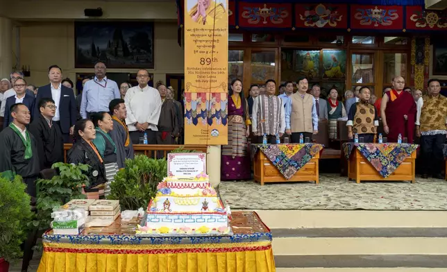 A large cake sits on a decorated table as Tibetan and Indian officials stand for their national anthems at an event to celebrate the 89th birthday of their spiritual leader the Dalai Lama at the Tsuglakhang temple in Dharamshala, India, Saturday, July 6, 2024. (AP Photo/Ashwini Bhatia)