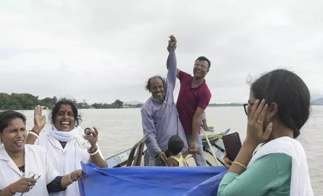 A member of a medical team holds up the hand of Kamaluddin as they celebrate the successful delivery of his newborn baby girl on a boat on her way to a health centre, over the River Brahmaputra, in the northeastern Indian state of Assam, Wednesday, July 3, 2024. (AP Photo/Anupam Nath)