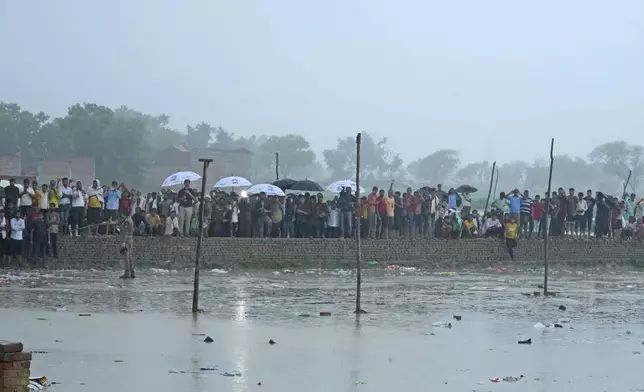 Villagers watch officials visit the site of Tuesday's stampede as it rains in Hathras district, Uttar Pradesh, India, Wednesday, July 3, 2024. Severe overcrowding and a lack of exits contributed to a stampede at a religious festival in northern India, authorities said Wednesday, leaving more than 100 people dead as the faithful surged toward the preacher to touch him and chaos ensued. (AP Photo/Rajesh Kumar Singh)