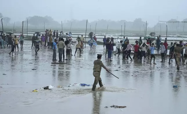 Police officers control a crowd that gathered at the site of Tuesday's stampede as it rains in Hathras district, Uttar Pradesh, India, Wednesday, July 3, 2024. Severe overcrowding and a lack of exits contributed to a stampede at a religious festival in northern India, authorities said Wednesday, leaving more than 100 people dead as the faithful surged toward the preacher to touch him and chaos ensued. (AP Photo/Rajesh Kumar Singh)