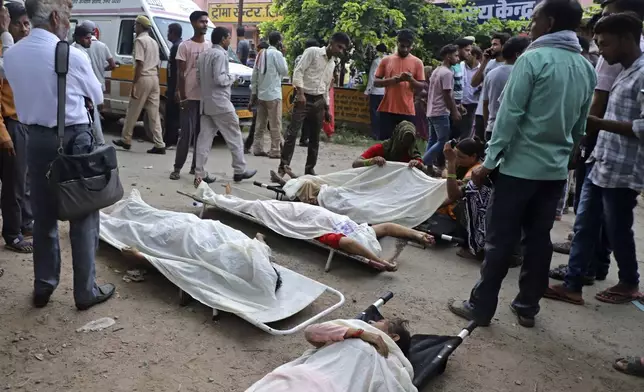 People stand around the bodies lying covered on stretchers outside the Sikandrarao hospital in Hathras district about 350 kilometers (217 miles) southwest of Lucknow, India, Tuesday, July 2, 2024. A stampede among thousands of people at a religious gathering in northern India has killed at least 105 and left scores injured, officials said Tuesday, with many women and children among the dead. (AP Photo/Manoj Aligadi)