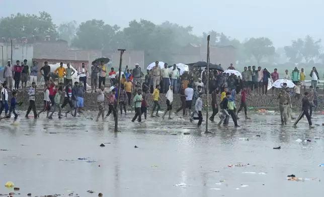 Villagers crowd at the site of Tuesday's stampede as it rains in Hathras district, Uttar Pradesh, India, Wednesday, July 3, 2024. Severe overcrowding and a lack of exits contributed to a stampede at a religious festival in northern India, authorities said Wednesday, leaving more than 100 people dead as the faithful surged toward the preacher to touch him and chaos ensued. (AP Photo/Rajesh Kumar Singh)
