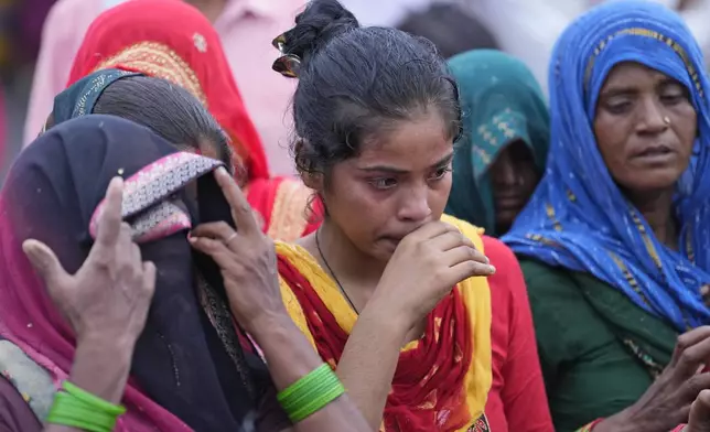 Villagers watch as family members prepare for the last rites of Savitri Devi, 50, who died during a stampede, in Ramnagar, in the northern Indian state of Uttar Pradesh, Wednesday, July 3, 2024. Devi was among more than 120 people who died in a stampede last week at a religious festival in northern India, as the faithful surged toward the preacher and chaos ensued among the attendees. (AP Photo/Rajesh Kumar Singh)