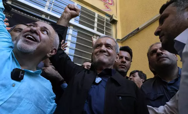 Reformist candidate for the Iran's presidential election Masoud Pezeshkian clenches his fist after casting his vote as he is accompanied by former Foreign Minister Mohammad Javad Zarif, left, at a polling station in Shahr-e-Qods near Tehran, Iran, Friday, July 5, 2024. Iranians are voting in a runoff election to replace the late President Ebrahim Raisi, who was killed in a May helicopter crash in the country’s northwest along with the foreign minister and several other officials. (AP Photo/Vahid Salemi)