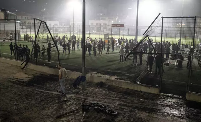 Residents and authorities stand at a soccer field that was hit by a rocket, killing multiple children and teenagers, in the Druze town of Majdal Shams, in the Israeli-annexed Golan Heights, Saturday, July 27, 2024. (AP Photo/Leo Correa)