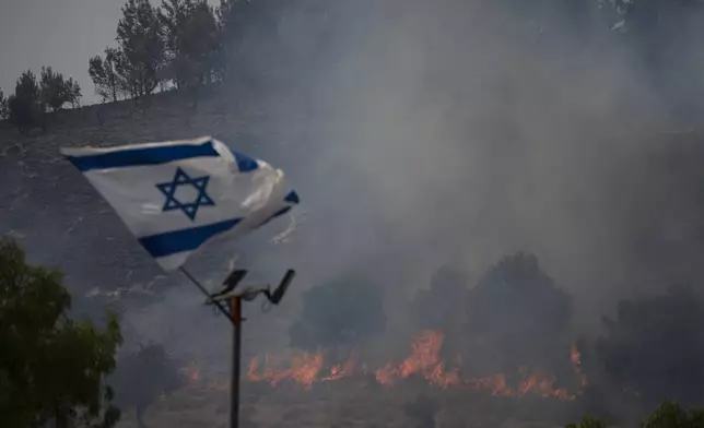 An Israeli flag flutters next to a fire burning in an area near the border with Lebanon, northern Israel in Safed, Wednesday, June 12, 2024. Scores of rockets were fired from Lebanon toward northern Israel on Wednesday morning, hours after Israeli airstrikes killed four officials from the militant Hezbollah group including a senior military commander. (AP Photo/Leo Correa, File)