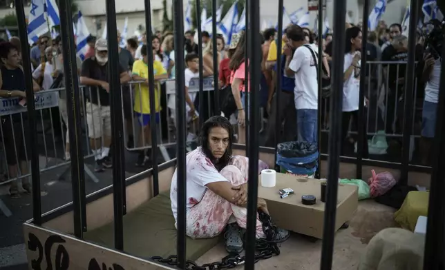 A woman sits in a cage during a protest marking nine months since the start of the war and calling for the release of hostages held in the Gaza Strip by the Hamas militant group, in Tel Aviv, Israel, Sunday, July 7, 2024. (AP Photo/Leo Correa)