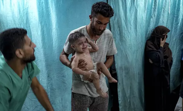 A Palestinian man holds a child wounded in the Israeli bombardment of the Gaza Strip in a hospital in Deir al-Balah, Thursday, July 18, 2024. (AP Photo/Abdel Kareem Hana)