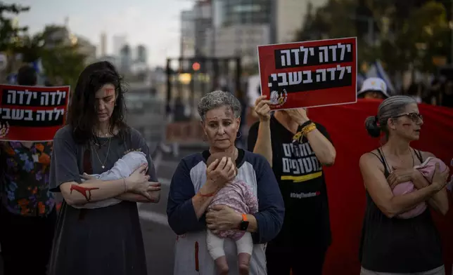 Relatives and supporters of Israeli hostages held by Hamas in the Gaza Strip hold baby dolls during a performance marking nine months since the start of the war and calling for their return, in Tel Aviv, Israel, Sunday, July 7, 2024. (AP Photo/Leo Correa)