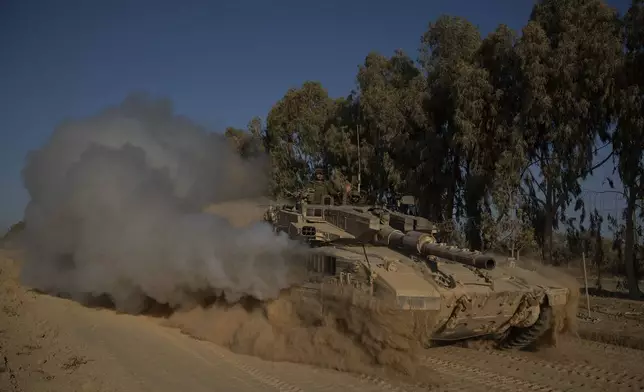 Israeli soldiers move on the top of a tank near the Israeli-Gaza border, as seen from southern Israel, Monday, July 8, 2024. Israeli forces advanced deeper into the Gaza Strip's largest city in pursuit of militants who had regrouped there, sending thousands of Palestinians fleeing on Monday from an area ravaged in the early weeks of the nine-month-long war. (AP Photo/Leo Correa)