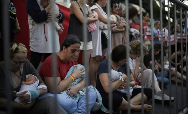 Relatives and supporters of Israeli hostages held by Hamas in the Gaza Strip hold baby dolls during a performance marking nine months since the start of the war and calling for their return, in Tel Aviv, Israel, Sunday, July 7, 2024. (AP Photo/Leo Correa)