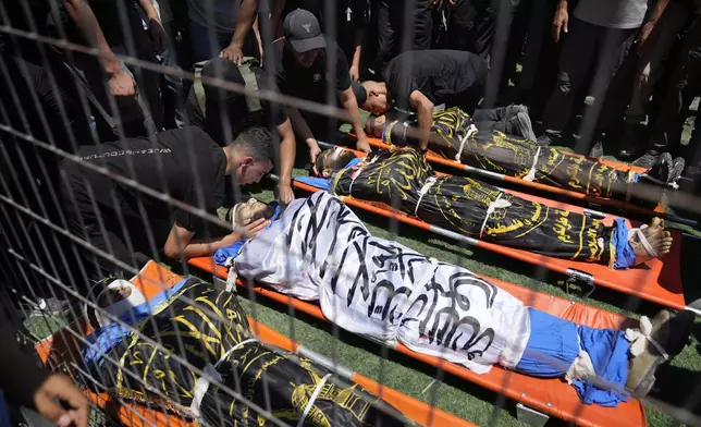 Mourners take the last look at the bodies, wrapped with Islamic Jihad flags of four Palestinians, who were killed by an Israeli airstrike late Tuesday, during their funeral in the West Bank refugee camp of Nur Shams, near Tulkarem, Wednesday, July 3, 2024. Palestinian health officials say four Palestinians were killed by an Israeli airstrike in a refugee camp in the northern West Bank late Tuesday. Israel's military said an aircraft struck a group of militants who were planting explosives in Nur Shams refugee camp near Tulkarem. (AP Photo/Nasser Nasser)