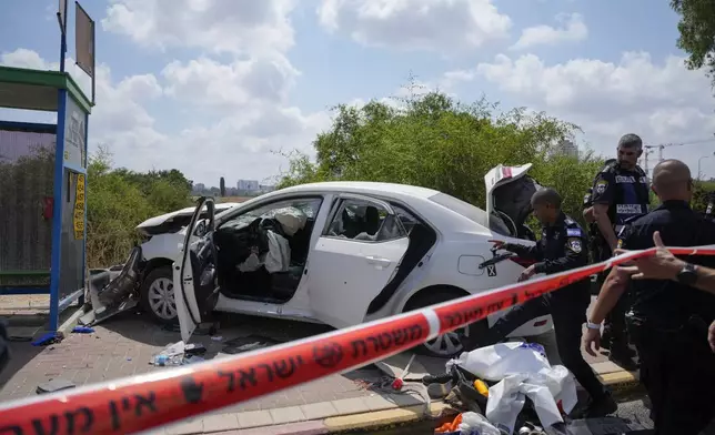 Israeli police officers work at the scene of a suspected ramming attack near Ramla, Israel, Sunday, July 14, 2024. According to the authorities a car slammed into pedestrians waiting at a bus stop, leaving at least four people injured. The suspect of the attack was shot and killed while still in his car. (AP Photo/Ohad Zwigenberg)