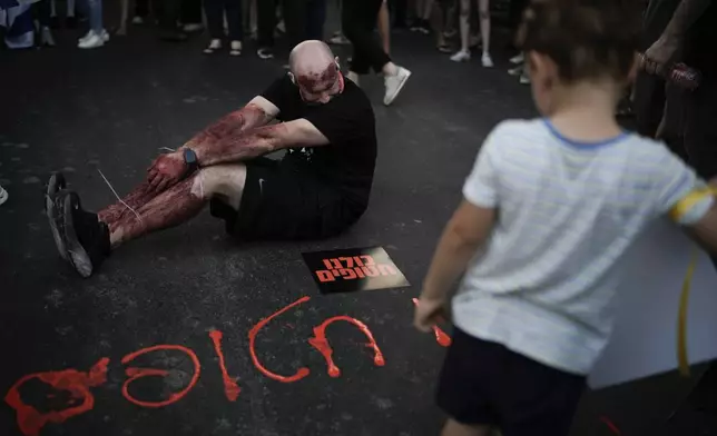 A man painted in red to symbolize blood during a protest marking nine months since the start of the war and calling for the release of hostages held in the Gaza Strip by the Hamas militant group, in Tel Aviv, Israel, Sunday, July 7, 2024. Hebrew on the ground reads, "We are all hostages". (AP Photo/Leo Correa)