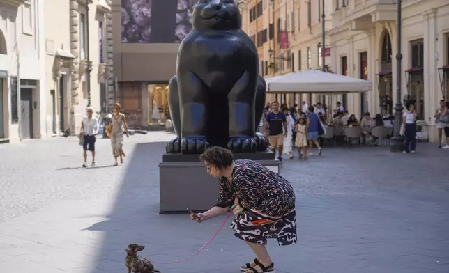 A woman takes a picture of her dog before Fernando Botero's "Cat" sculpture at Rome's Piazza San Lorenzo in Lucina on Saturday, July 20, 2024. Rome's storied streets and piazzas have become a vibrant canvas for Botero's exuberant sculptures, turning the city into an open-air museum of voluminous forms and daring artistry. (AP Photo/Gregorio Borgia)