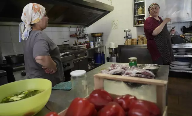 Ruqaia Agha, a Palestinian woman from Ramla, right, talks to Jumana Farho, from Syria, as they work in the HummusTown kitchen in Rome, Saturday, July 27, 2024. A pair of Syrians have created community that provides support to migrants and vulnerable people in Rome, by sharing the flavors of a homeland torn by civil war. Created in 2018 as a "humanitarian catering service," HummusTown originally aimed at raising funds for families and friends in Syria. (AP Photo/Gregorio Borgia)